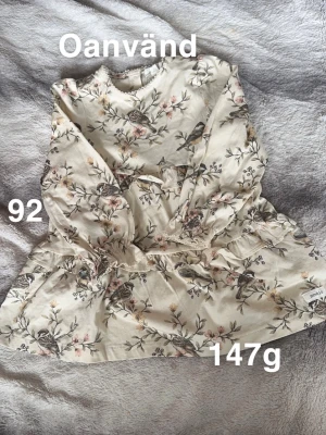 Blommig klänning från Newbie stl 92 - Supersöt ljus klänning från Newbie med blommigt mönster och små fåglar. Klänningen har lång ärm, volangdetaljer i midjan. Perfekt för vår och sommar!🌸 Oanvänd. Storlek 92