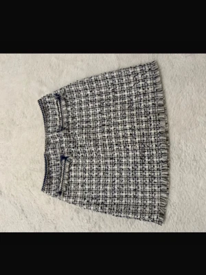 Rutig kortkjol i tweedstil - Säljer en snygg rutig kortkjol i svart och vitt med fransad nederkant. Kjolen har en klassisk tweedlook och två dekorativa fickor framtill. Perfekt att styla med strumpbyxor och sneakers för en trendig vibe.