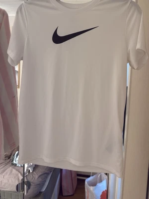 Vit Nike Dri-Fit t-shirt - Säljer en clean vit Nike t-shirt. Tillverkad i Dri-Fit material som andas och känns lätt på kroppen. Klassisk passform med rund hals och korta ärmar, perfekt för träning eller chill.
