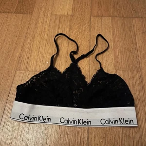 Svart spetslinnetopp Calvin Klein - Svart spetslinnetopp från Calvin Klein med smala  Toppen är ärmlös och har en feminin spetsdetalj som ger en snygg look. Perfekt att bära under en skjorta eller som den är