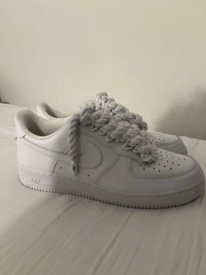 Nike Air Force 1 med chunky snören - Nike Air Force 1 sneakers i helvitt skinn med extra tjocka, rep-liknande snören för en unik och trendig look. Klassisk perforerad tå och låg profil. Perfekta för dig som vill sticka ut med dina skor.