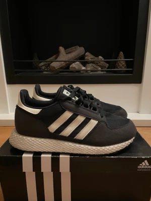 Svarta Adidas sneakers med vita detaljer - Säljer ett par svarta Adidas sneakers med klassiska vita ränder och logga på hälen. Skorna har snörning, mesh- och mockadetaljer samt en unik mönstrad sula. 
