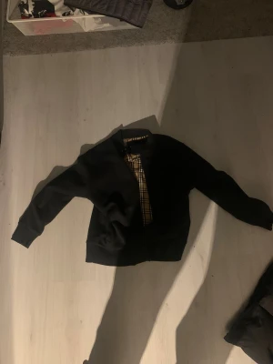 Svart stickad  från Park Lane XXL - Svart stickadjacka från Park Lane Jackan har ett klassiskt rutigt foder i beige och svart, ribbade muddar vid ärmslut och midja samt en stilren, enkel design. Perfekt för dig som gillar tidlös streetstil och vill ha en jacka med snygga detaljer.Storlek xxl men sitter som en L.Finns inte att köpa mer väldigt sällsynt jacka att hitta.