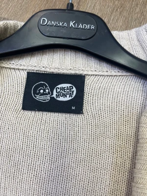Beige kofta från Cheap Monday M - Snygg beige kofta från Cheap Monday i storlek M. Den är stickad i mjukt material och har bred ribbad krage, två stora ribbade fickor framtill och knäppning med vita knappar. Perfekt för dig som gillar chill och enkel stil.
