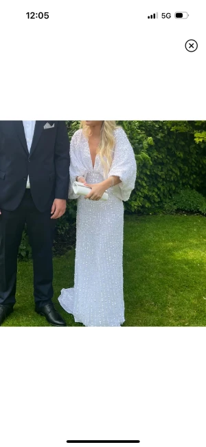 Vit långklänning med paljetter - Säljer en vit långklänning med glittriga paljetter och v-ringad front. Helt slutsåld överallt! Klänningen har ballongärmar, öppen rygg och dragkedja bak. Den är i storlek S. Jag är ca 160 men klänningen passar även folk som är längre. Klänningen är lite smutsig under släpet då den har används till bal men är ingenting som syns. (Köpt här på plick!) lånade bilder