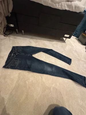 Replay mörkblå slim jeans storlek 33 - Snygga mörkblå jeans från Replay med klassisk femficksdesign och diskreta slitningar. Modellen är slim med raka ben och har detaljerade sömmar på bakfickorna samt Replay-logga på linningen. Perfekt för dig som gillar stilrena och moderna jeans.