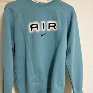 Blå Nike Air sweatshirt i medium - Nike Air sweatshirt i en snygg blå färg med stort AIR-tryck och liten svart swoosh på bröstet. Tröjan har lång ärm, rund hals och är gjord i mjuk bomullsmix. Perfekt för dig som gillar streetwear och sportig stil.