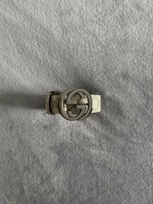Gucci bälte  - Säljer ett beige Gucci GG Supreme bälte med klassiskt monogrammönster och stor silverfärgad GG-logga som spänne. Bältet är tillverkat i skinn med canvas på ovansidan och har en stilren, lyxig vibe som lyfter vilken outfit som helst.