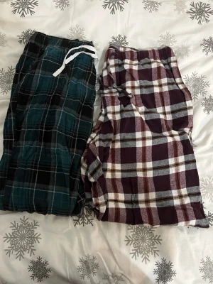 Två par rutiga mjukisbyxor med snörning - Säljer två par mjukisbyxor med rutigt mönster och snörning i midjan. Ena paret är mörkgrön och svart, det andra är vinröd, vit och brun. Perfekta för chill hemma eller när du vill vara extra bekväm. Båda har elastisk midja och är gjorda i mjukt bomullsmaterial.