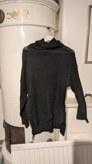 Svart stickad polotröja - Svart stickad polotröja med lång ärm och bred krage. Tröjan har en loose passform och ribbade detaljer vid nederkant och ärmslut. Perfekt för kyliga dagar och enkel att matcha med jeans eller kjol.