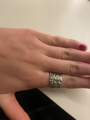 Bred silverfärgad ring med hamrad yta - Säljer en bred och chunky ring i silverfärg med cool hamrad och ojämn yta. Ringen är öppen baktill vilket gör den justerbar i storlek. Perfekt för dig som gillar statement-smycken med lite edge och unik struktur. Rostar inte!