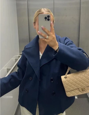 Mörkblå skepparkavaj med bred krage - Snygg mörkblå skepparkavaj med bred krage och dubbelknäppning framtill. Jackan har långa ärmar och klassisk, rak passform. Perfekt för dig som gillar stilrena och tidlösa plagg med lite marint vibe.