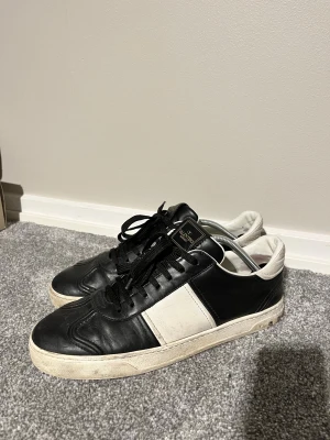 Valentino flycrews svartvita i läder - Svarta och vita sneakers från Valentino med snygg kontrastpanel och klassisk rund tå. Skorna har svart snörning, platt sula med mönstrad undersida och är tillverkade i skinn. Perfekt för dig som gillar stilrena och lyxiga sneakers med en modern vibe.                                                        19/22 nitar kvar och tvättar dem innan jag skickar iväg dem.                                                 SJÄLVKLART ÄKTA KÖPTE FRÅN VESTIAIR✅