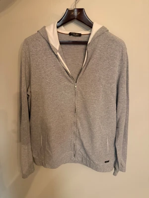 Loro Piana zip hoodie  - Snygg grå hoodie från Loro Piana med vit insida på huvan och hel dragkedja framtill. Tröjan har långa ärmar, två fickor och en stilren look.