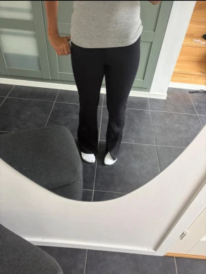 Svarta bootcut byxor med slits - Säljer ett par svarta bootcut byxor med slits vid bensluten. De har hög midja och är gjorda i ett mjukt, stretchigt material som sitter snyggt och bekvämt. Perfekta om du gillar en stilren look med lite edge. Passar dig som vill ha en modern siluett.