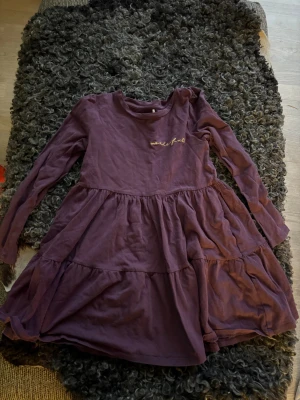 Lila volangklänning med matchande tuffa leggings NAME IT  - Säljer en plommonlila klänning från NAME IT med volanger och lång ärm. Klänningen har ett broderat gult texttryck 'wonderful' på bröstet och är tillverkad i mjuk bomull. Passformen är normal och modellen är ”volang” klänning till knäna med rund hals. Matchande, tuffa leggings i samma material ingår i priset. 