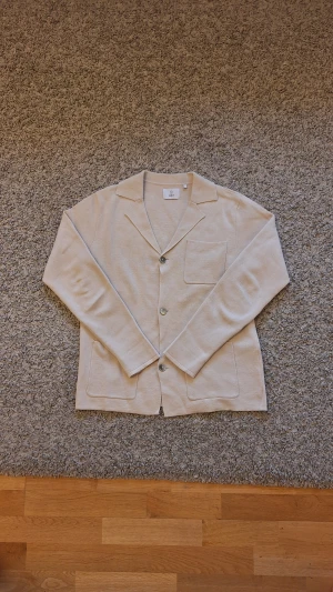 Beige stickad kavaj cardigan från Bläck - Beige stickad kavaj cardigan från Bläck i storlek M(passar S också). 100% bomull. Använd fåtal gånger och skicket är i princip som ny, inga slitningar eller defekter finns. Den har tre fickor samt tre knappar. Jättesnygg för en stilig outfit för alla olika sorters tillfällen. Skick: 9/10