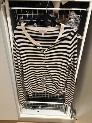 Randig kofta från H&M i svart och vit - Snygg randig kofta från H&M i storlek M. Koftan har svarta och vita horisontella ränder, rundad hals och knappar framtill. Långärmad och tillverkad i mjuk stickad bomull, perfekt för lager på lager. 