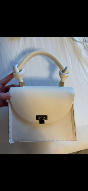 Beige handväska - En beige handväska. Denna är använd och är repig på gulddetaljen. Kommer med ett långt band. Den har knytningar i handtaget som är väldigt fint. 