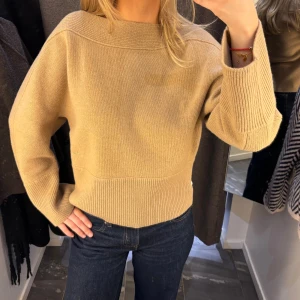 Beige stickad tröja från Dagmar - Snygg beige stickad tröja från Dagmar med bred ribbad kant vid hals, ärmslut och nederkant. Modellen är loose fit med långa ärmar och en stilren, enkel design som är lätt att matcha. Perfekt för dig som gillar klassiska och trendiga plagg.