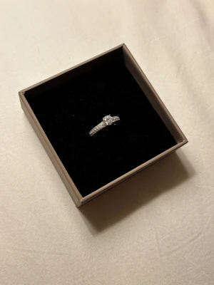 Silverring med glittrande stenar - Snygg silverring i äkta 925 silver med en rund, gnistrande sten i mitten och små glittriga stenar längs hela bandet. Perfekt för dig som gillar bling och vill ha något som verkligen syns. Ringen har en klassisk och elegant design som passar till alla stilar. Säljes i originalbox, bild tre