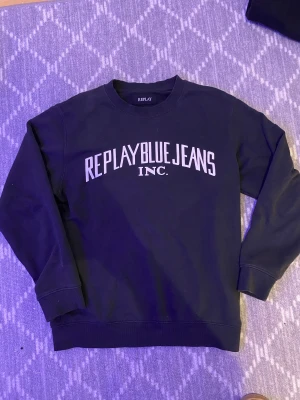 Svart sweatshirt från Replay Blue Jeans - Cool svart sweatshirt från Replay Blue Jeans med vit tryckt logga på bröstet. Tröjan har rund hals, ribbade muddar vid ärmar och nederkant samt långärmad passform. Perfekt för dig som gillar streetwear och enkel stil.🤟🏽🤟🏽