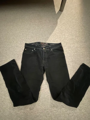 Svarta manchesterbyxor Jacob Cohën - Snygga svarta manchesterbyxor från Jacob Cohën med klassisk femficksdesign och silverfärgade detaljer. Byxorna har rak passform och är tillverkade i mjuk manchester med exklusiv känsla. Perfekt för dig som gillar stilrena och tidlösa plagg.