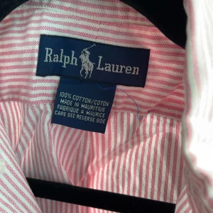Rosa och vit randig skjorta Ralph Lauren - Säljer en klassisk skjorta från Ralph Lauren i rosa och vitt randigt mönster. Skjortan är i 100% bomull, har knappar framtill och den ikoniska broderade loggan på bröstet. Perfekt för en stilren och avslappnad look.