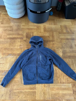 Marinblå hoodie från Sail Racing - Marinblå hoodie från Sail Racing i storlek M. Tröjan har hel dragkedja framtill, huva och en bröstficka med dragkedja. 