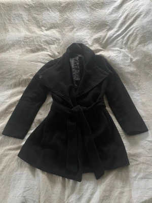Svart kappa med bälte och krage - Stilren svart kappa med bred krage och knytskärp i midjan. Funkar bra till höst och vinter. 