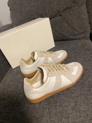 Maison Margiela Gats - Maison Margiela gata skor i vitt och beige med klassisk gummisula. Ovandel i skinn och mocka, neutrala färger och snygga detaljer. Perfekta för dig som gillar minimalistisk och clean stil. Hör av er vid minsta lilla fundering😊
