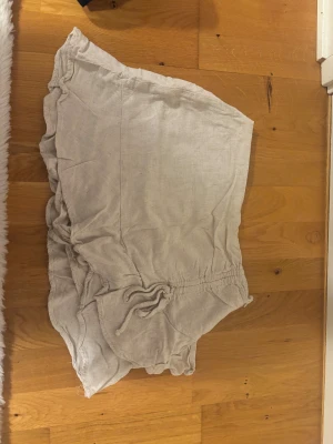 Beige linneshorts/kjol med volangkant - Säljer ett par ljusbeige kjol-shorts i linne med snygg volangkant och snörning i midjan. Perfekta för varma dagar och har en skön loose passform. Superfina att matcha med en enkel topp eller hoodie.