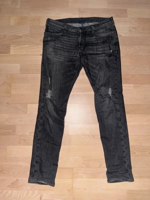 Gråa slim fit jeans från Armani, W32 L34 - Svarta jeans från Armani med slim fit passform och snygga slitningar på benen. Klassisk femficksmodell med silverfärgad Armani-logga på bakfickan. Jeansen har låg midja och är tillverkade i stretchigt bomullsmaterial för skön komfort. Pris kan diskuteras 