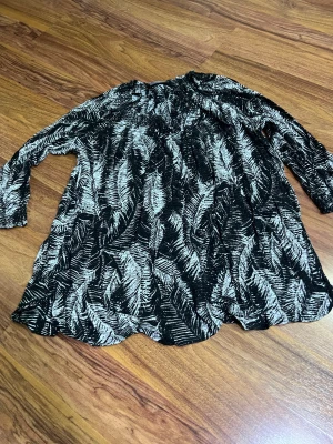 Svartvit mönstrad klänning från Violeta - Svartvit kortklänning från Violeta med coolt abstrakt mönster, långa ärmar och avslappnad passform. Klänningen har smockad halsringning och dekorativa knytband med tofsar. Tillverkad i mjuk viskos som känns skön mot huden.