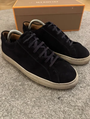 Marinblå mockasneakers från Myrqvist - Snygga navy blue sneakers från Myrqvist i mjuk mocka med rund tå och platt vit sula. Klassisk låg modell med snörning och diskret design som passar till jeans eller chinos. Insidan är fodrad i ljust skinn för extra komfort. Perfekt för dig som gillar stilrena och tidlösa skor. Mycket bra skick och inga defekter, undersulan är  lite skitig men helt felfri utöver det. Nypris: 2000kr Hör av dig vid frågor.
