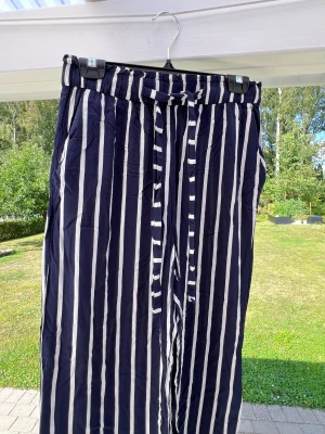 Marinblå/vit randiga flow byxor från H&M - Randiga flowy byxor från H&M med knytband och stretch i midjan. Knappt använda 💙 Storlek 40  Innerbenslängd: 70 cm Midja: 76 cm