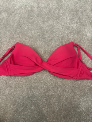Rosa bikiniöverdel från NLY Beach - Säljs då den är för liten för mig. Snygg rosa bikiniöverdel från NLY Beach med twistad front och vadderade kupor. Modellen har smala axelband och är tillverkad i mjuk polyester och elastan för en skön passform. Perfekt för strandhäng och poolparty i sommar!