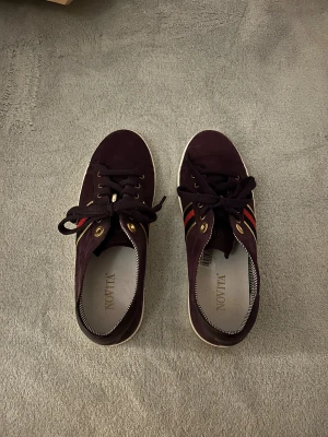 Mörklila sneakers från Novita - Endast använda 1 gång! Sneakers Novita med gulddetaljer och svarta samt röda ränder på sidan Perfekt för dig som gillar stilrena och färgstarka sneakers.