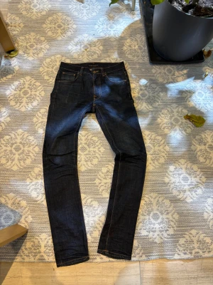 Nudie Jeans Lean Dean mörkblå W30 L34 - Säljer ett par Nudie Jeans Lean Dean i mörkblå tvätt, modellen är slim med raka ben och klassiska orange sömmar. Materialet är 98% ekologisk bomull och 2% elastan för extra stretch. Snygga detaljer och stilren look.