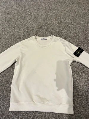 Stone Island Sweatshirt Strlk M - Hej! Säljer min Stone Island Sweatshirt i Strlk M. Den är i mycket bra skick förutom att ”Stone Island” loggan har släppt i kragen som man kan se på 4:e bilden, men det går att sy fast igen enkelt. Använd ett fåtal gånger. Nypris: 4299kr, mitt pris: 999kr. Pris kan diskuteras! 
