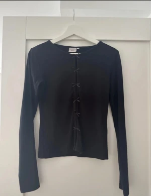 Svart långärmad topp med snörning - Svart långärmad topp från Bik Bok med snörning framtill som ger en cool detalj. Modellen är slim och har en rund halsringning. Perfekt för dig som gillar minimalistisk stil med en twist. Materialet känns mjukt och stretchigt mot huden.