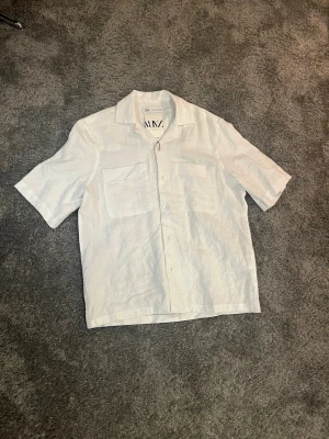 Vit linneskjorta från Zara, S - Fräsch vit skjorta från Zara i storlek S, tillverkad i linne. Skjortan har korta ärmar, klassisk krage och två stora bröstfickor framtill. Perfekt för en chill och stilren look under varma dagar. Knappar framtill för enkel stängning. Den är helt oandvänd och tagsen är kvar passar dig som är ca 170-180