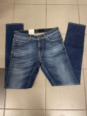 Slim fit blå Tiger of Sweden  jeans W29 L34 - Slim fit jeans i klassisk blå tvätt med snygga slitningar och kontrastsömmar. Modellen har fem fickor, bälteshällor och läderpatch bak i midjan. Perfekta jeans för dig som gillar en smalare passform och stilren look.