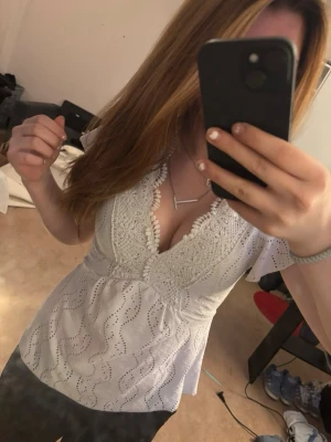 Vit blus med spets och v-ringning - Säljer en vit blus med v-ringad spetskant och broderade detaljer. Blusen har korta ärmar och ett vågigt hålmönster över hela tyget. Tror den e köpt utomlands ❤️