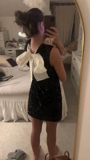 Svart glittrig kortklänning med rosett - Supersöt svart glittrig kortklänning med stor vit rosett i ryggen. Klänningen är ärmlös och har en rak, lite loose passform. Perfekt nu till nyår!  Den är i storlek XS och oanvänd med prislappen kvar💞💞 Fri frakt just nu så passa på!