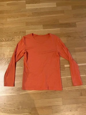 Orange långärmad topp - Snygg orange långärmad topp med rund halsringning i tunn ull. Enkel och stilren design som funkar till många olika looks. Mjuk och skön känsla, perfekt att ha som basplagg. Passar dig som gillar färg och vill sticka ut lite extra.