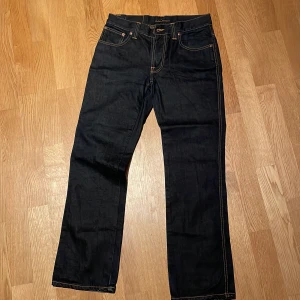 Blå  jeans från Nudie Jeans - Snygga blå  jeans från Nudie Jeans med klassisk femficksdesign och kontrasterande sömmar. Perfekta för en stilren look. De har en knappgylf och är tillverkade i slitstarkt denim. Storlek 31/32