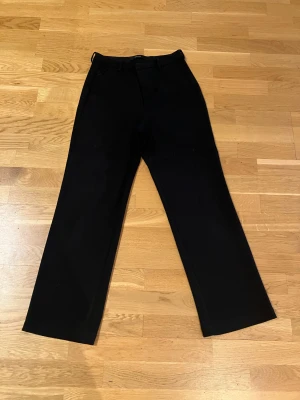 Svarta kostymbyxor med raka ben - Snygga svarta kostymbyxor med klassisk rak passform och pressveck. Byxorna har hällor för bälte och diskreta sidofickor. Perfekta för en clean och stilren look. Materialet känns mjukt och har en lätt stretch för extra komfort.
