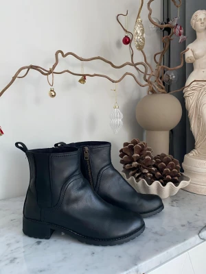 Timberland boots stl 38 – svarta, stil & komfort - Säljer ett par Timberland boots i storlek 38 – dam, svarta med dragkedja. Bootsens skick är mycket fint. Kombinerar stil, komfort och kvalitet i ett – perfekt för kontoret, AW:n, festen eller vardagsäventyren. Robust design möter sofistikerad look som passar både till jeans, kjol eller klänning. En sko som verkligen gör skillnad både i vardag och när du vill lyfta din stil. Notera: Liten nagg - Syns om man tittar nära, men inget som syns på håll. (Se sista bild) 