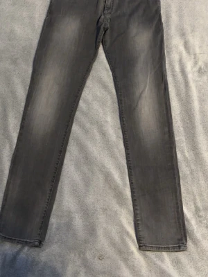 Grå jeans från Tommy Hilfiger - Snygga grå jeans från Tommy Hilfiger med klassisk femficksdesign och diskret logga på bakfickan. Jeansen har en rak passform och är tillverkade i mjukt denimtyg som ger en skön känsla. Perfekt för dig som gillar stilrena och tidlösa plagg.